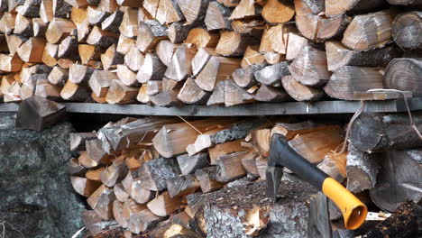 Man-swings-axe-and-splits-log-in-slow-motion-against-wood-stockpile-background