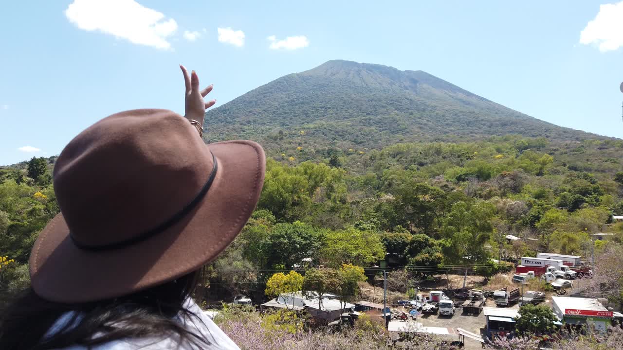 Donna viaggiatrice in posa in un punto panoramico con il vulcano Chaparrastique sullo sfondo, El Salvador, turismo in America Centrale