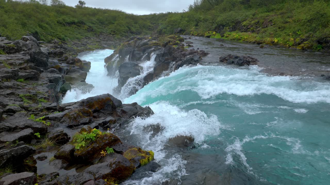 río con una poderosa cascada cerca del bosque y entre las rocas negras