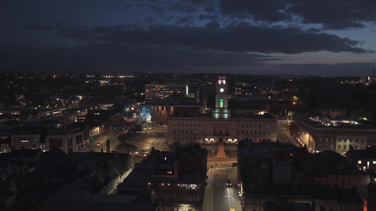 Veduta aerea notturna del Municipio di Barnsley e del paesaggio urbano circostante a Barnsley, South Yorkshire, Inghilterra, con strade e skyline illuminati, ripresa con drone in scorrimento laterale con panoramica a sinistra.