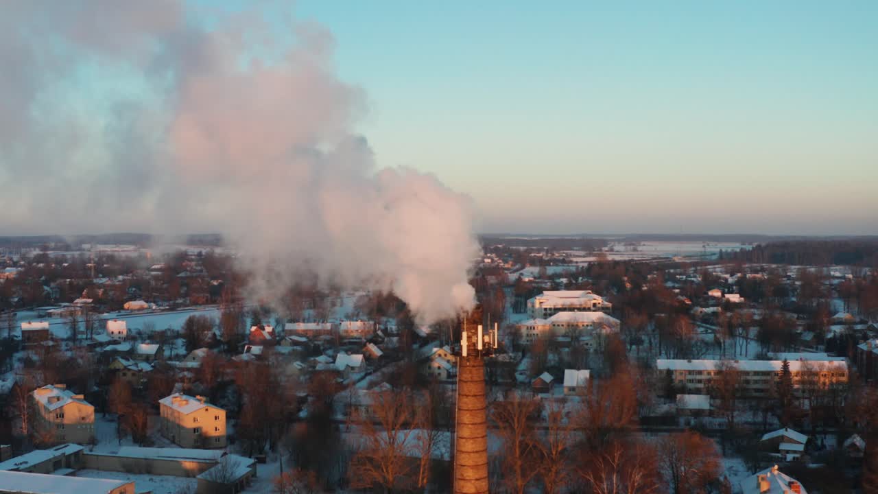 la chimenea de producción de calor iluminada por el atardecer en la ciudad emite humo en la atmósfera