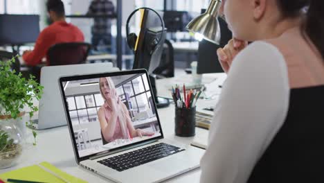 mujer caucásica haciendo una videollamada con una colega en una computadora portátil en la oficina