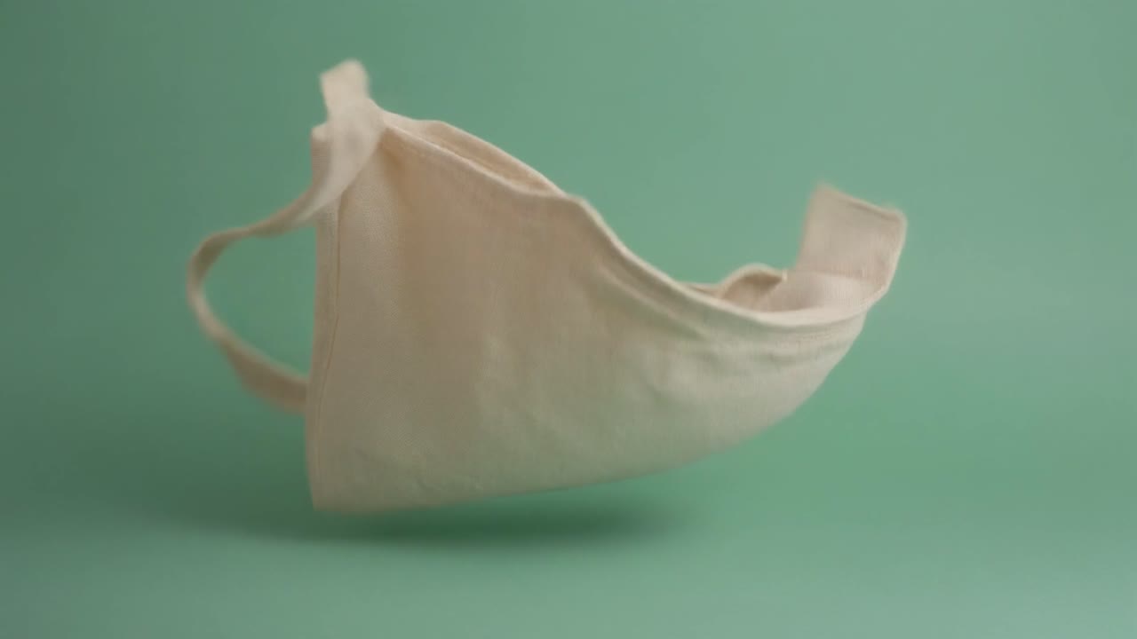 Borsa tote in tessuto beige che cade e si dispiega su sfondo verde
