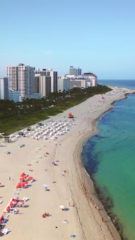 vertical aerial over south beach, miami, moving from the shore into the turquoise ocean, unveiling the iconic coastline lined with white sands, swaying palms,and a row of luxury resort hotels.