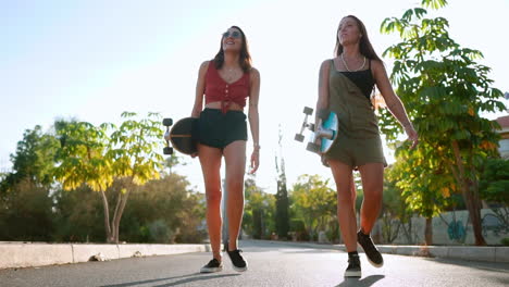 girls carry skateboards to the park near palm trees, sharing conversation, laughter, and smiles, their camaraderie illuminated by the setting sun in slow motion