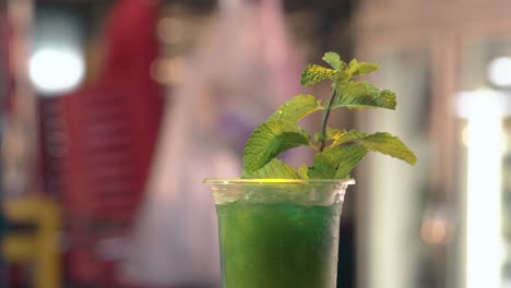 green cocktail with fresh mint against blurry market and man