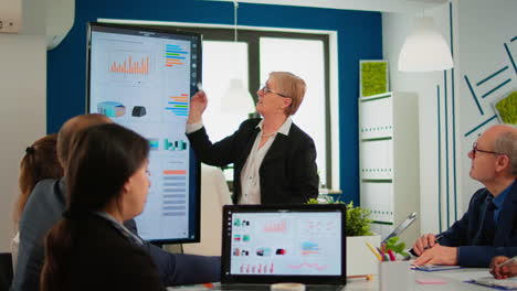 elderly project manager pointing at desktop presenting statistical data,