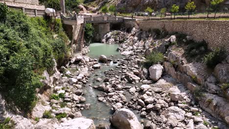 Panoramic-Aerial-shot-of-stony-river-bed-and-water-flowing-through-rocks