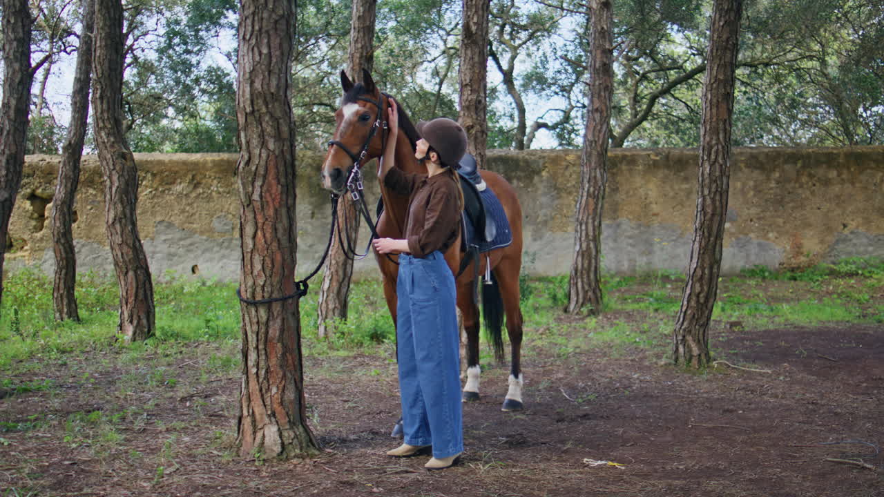 Young equestrienne caressing horse at farm. Happy cowgirl looking camera ranch