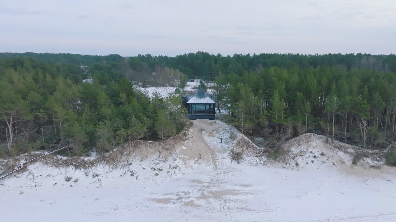 vista aérea de la costa del mar báltico en un día de invierno nublado, una pequeña casa de vacaciones gris en la playa con arena blanca, erosión costera, cambios climáticos, amplio tiro de drones retrocediendo
