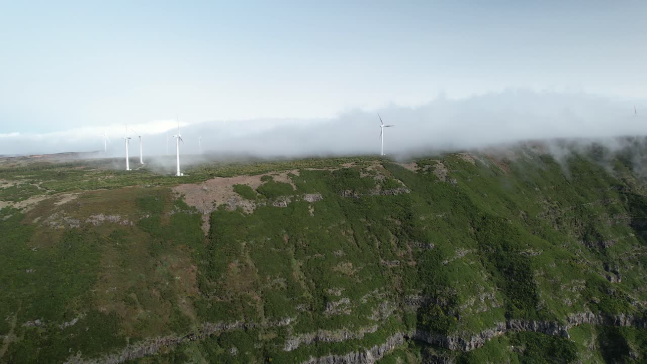 울창한 녹색 마데라 산꼭대기 위의 구름은 회전하는 풍력 터빈을 고 있습니다.