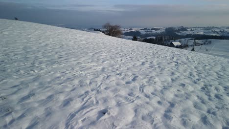 Drone-flying-over-a-wintry,-hilly-landscape-in-rural-Switzerland