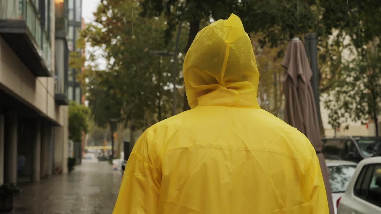 Business man tourist person with umbrella and raincoat on rainy european city street, lights reflecting, walking in Barcelona or Amsterdam during the rain