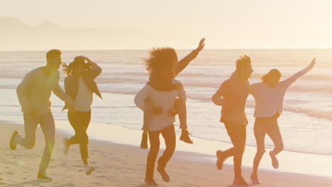 un grupo de amigos divirtiéndose corriendo a lo largo de la playa de invierno juntos