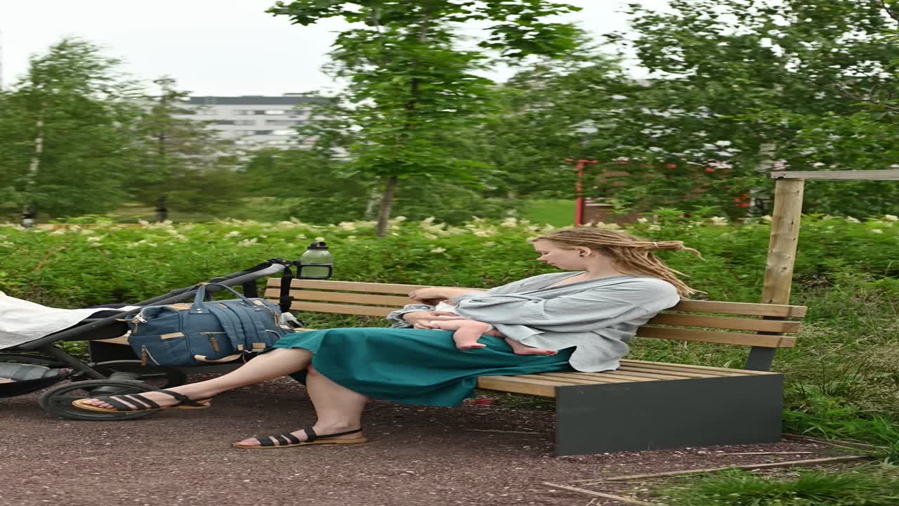 Kvinde med baby og barnevogn sidder på en bænk i en park.
