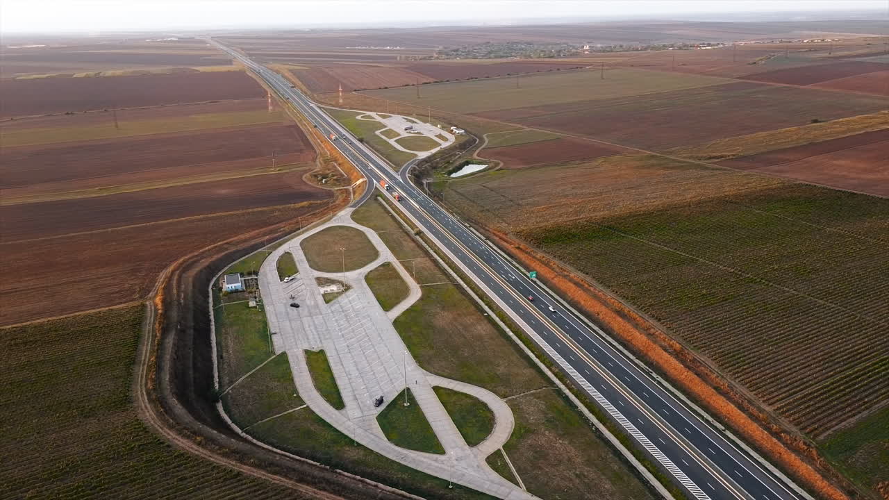 The Motorway of the Sun with moving cars and parking on the side of the road, fields around. View from the drone. Romania