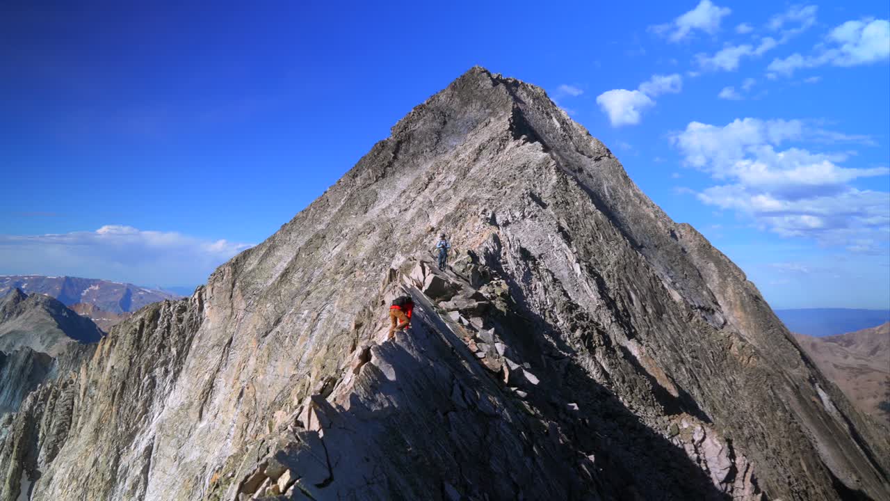 Knifes Edge Capitol Peak north east ridge Wilderness Trail Hikers scrambling rock climbing across Rocky Mountains Colorado 14er mountainside large boudlers aerial view summer blue sky morning zoom in