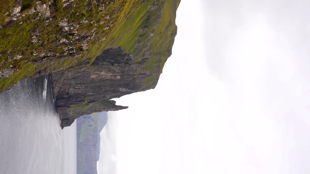 Ripresa con inclinazione verso il basso di Trollkonufingur che emerge dall'oceano accanto a scogliere a Vagar, Isole Faroe