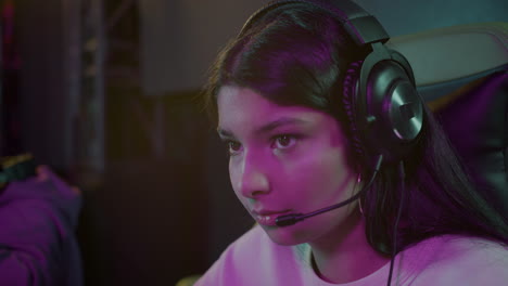 close up of a happy cybersport female gamer playing video games while sitting with her friends in gaming club