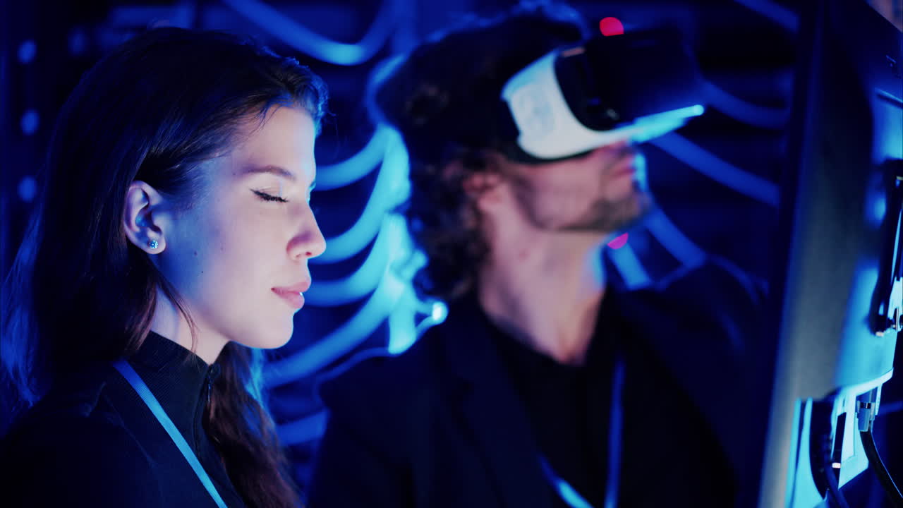 Woman programming in a server room while a man is using a Virtual Reality headset