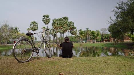 man with bicycle by a pond in a scenic thai historical park