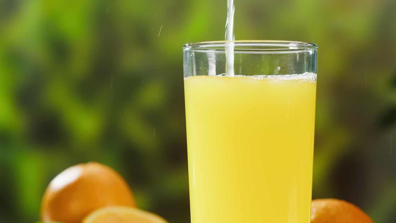 Suco de laranja fresco sendo servido em um copo com frutas cítricas