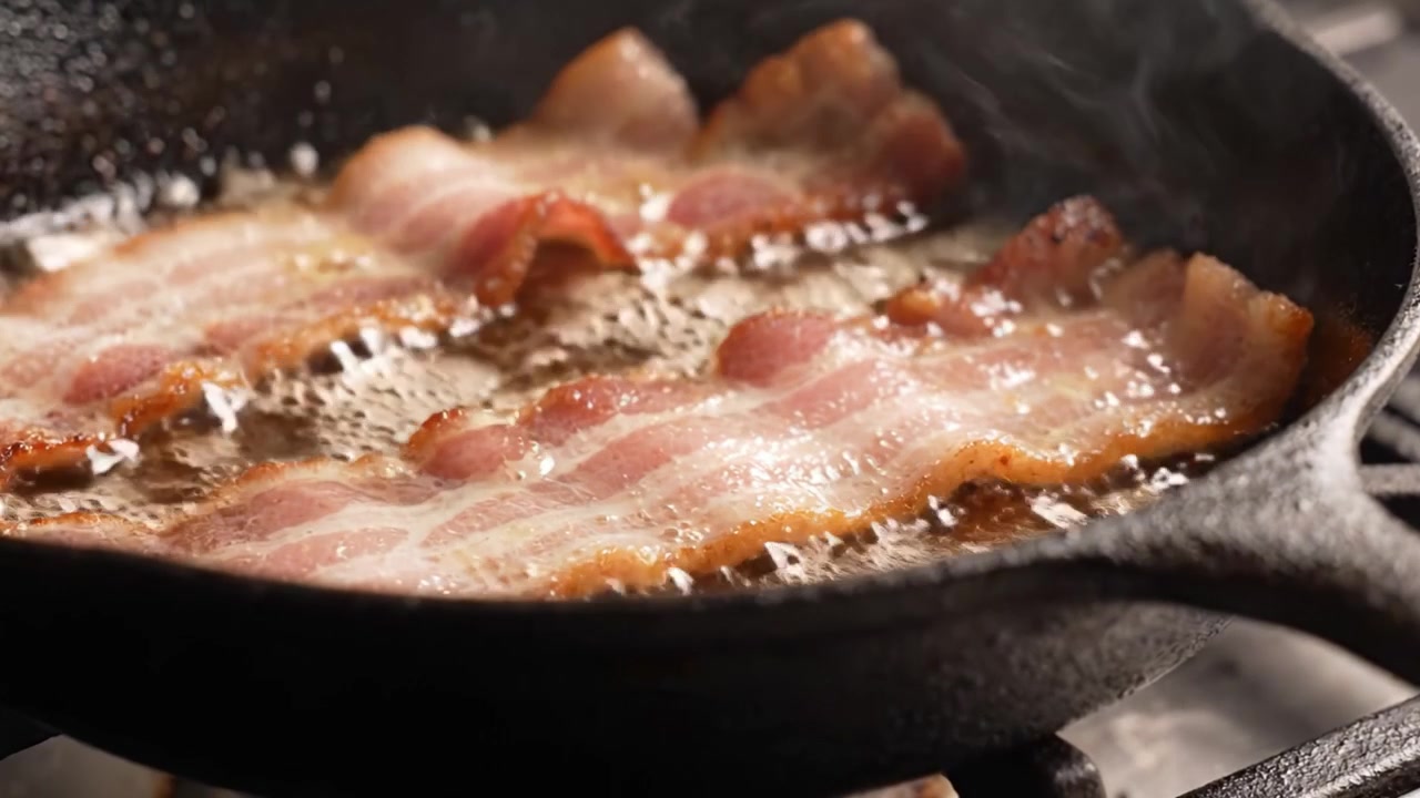 Pancetta sfrigolante in una padella di ghisa: cattura la consistenza e il sapore perfetti mentre cuoce fino a una croccante perfezione con bordi dorati.