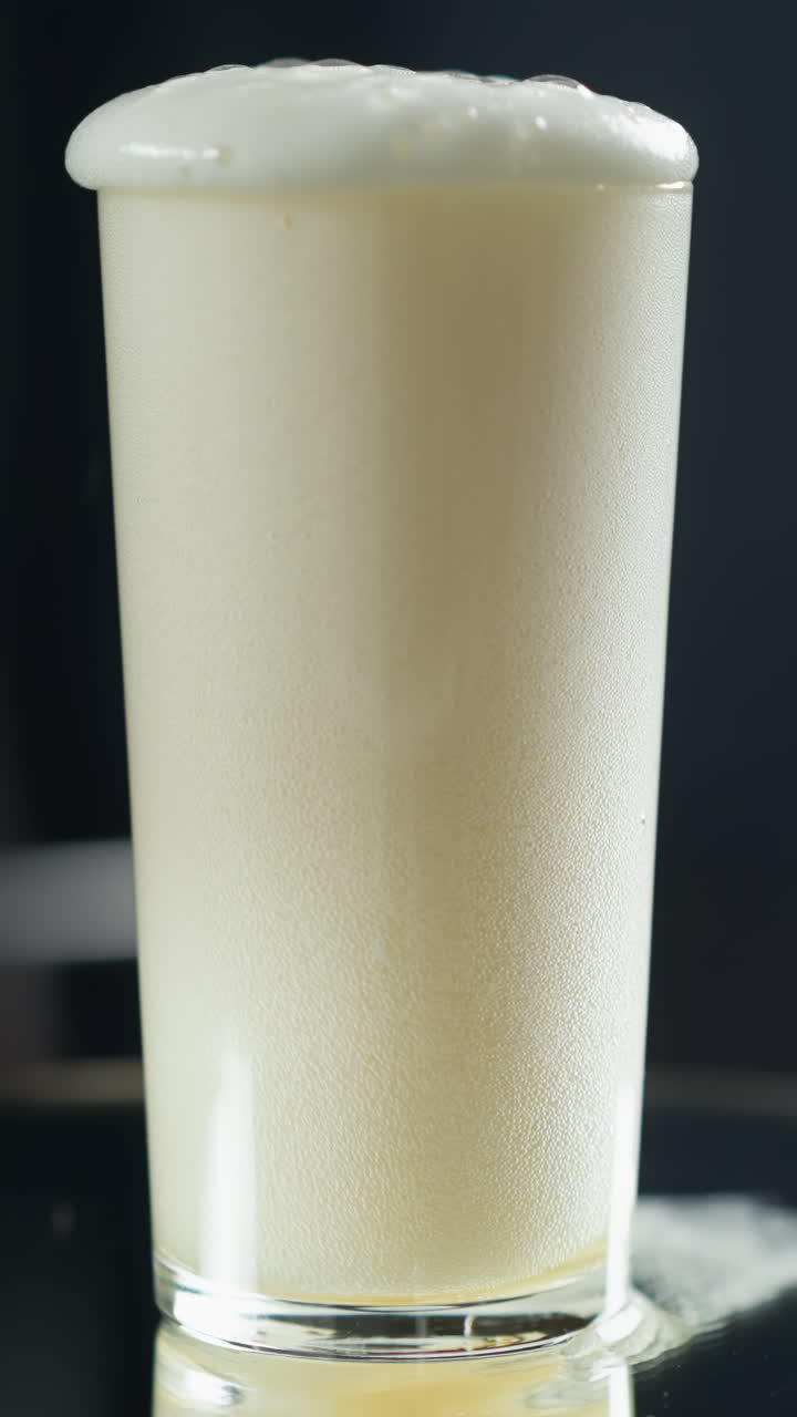 Creamy liquid cascading into a tall glass, creating a frothy swirl against a dark backdrop