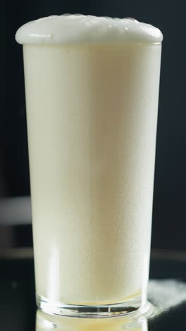 líquido cremoso en cascada en un vaso alto, creando un remolino espumoso contra un fondo oscuro