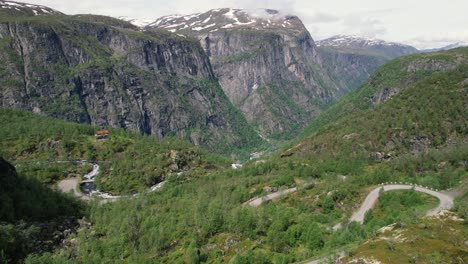 Vista-Aérea-De-La-Sinuosa-Carretera-De-Montaje-En-El-Parque-Nacional-De-Hardangervidda-Con-Enormes-Acantilados-En-El-Fondo