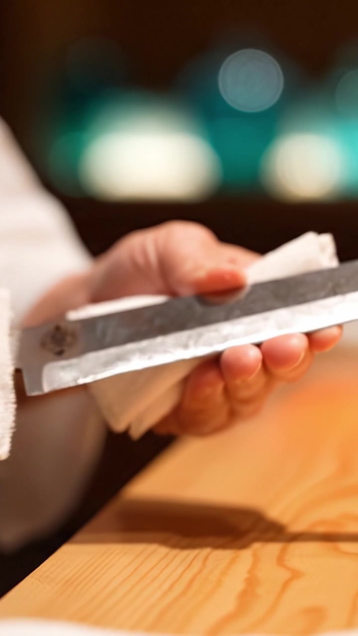A close-up view of a hand elegantly holding a kitchen knife wrapped in a cloth, showcasing careful handling and an artistic culinary presentation.