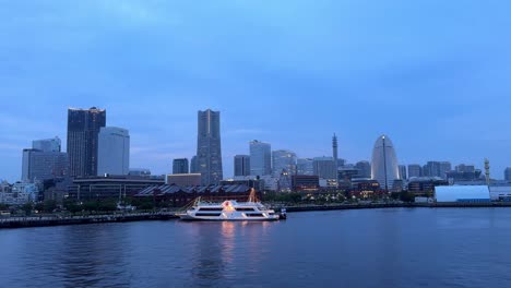 twilight cityscape with a yacht on the water, skyline illuminated, tranquil urban scene, dusk