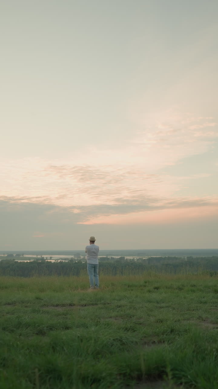 색 셔츠, 모자, 청바지를 입은 성인 남성이 해가 지는 동안 조용한 호수 에 있는 잔디 에서 상하고 서 있다.