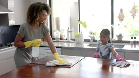 happy biracial mother and daughter cleaning kitchen worktop together, slow motion