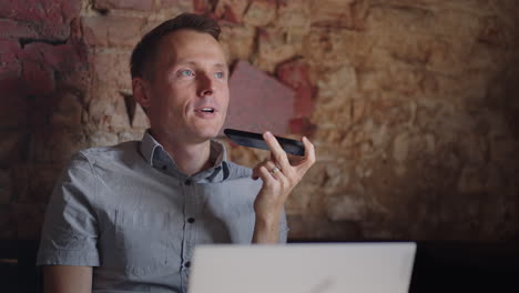 smiling young man recording voice recognition message on speakerphone. businessman using virtual assistant app sets reminder on smart phone at home office. digital ai mobile assistance tech concept