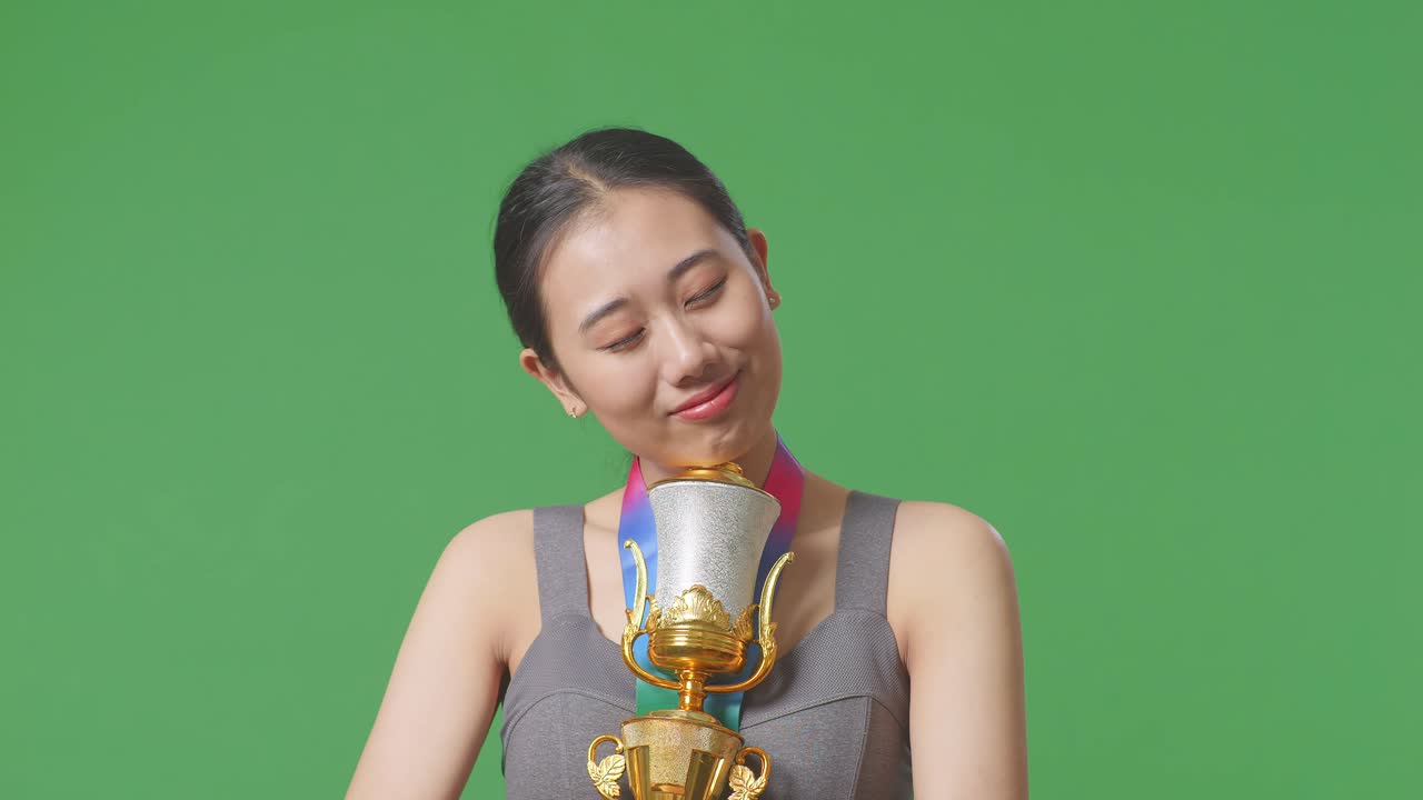 금메달을  아시아 여성이 황금 트로피를 안고 자랑스럽게 첫 번째 우승자로 우승하는 녹색 스크린 배경에서 스튜디오에서