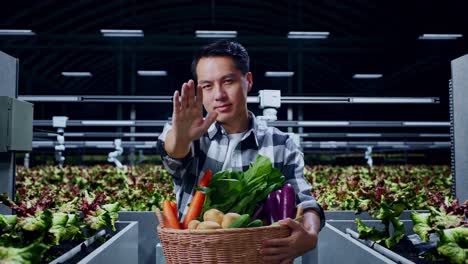 granjero masculino asiático con una canasta de verduras que muestra una parada, un letrero tabú, de pie en una granja inteligente