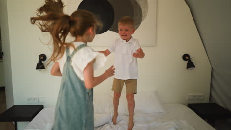 los niños juegan activamente en la cama en glamping. niño pequeño sonriente agarra las manos de la hermana saltando en el colchón en el dormitorio. niños felices en la tienda de vacaciones