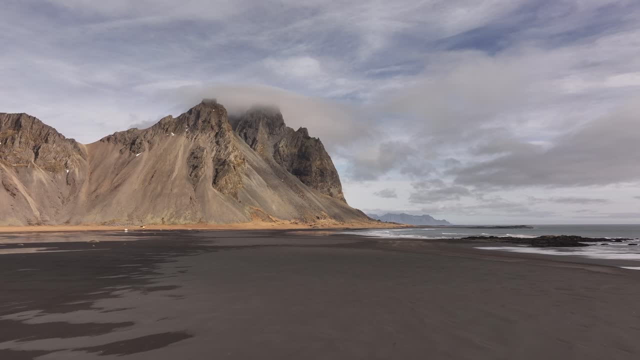 Vestrahorn mountain and volcanic black sand beach in Iceland drone view, cloudy sky, remote Arctic beauty.