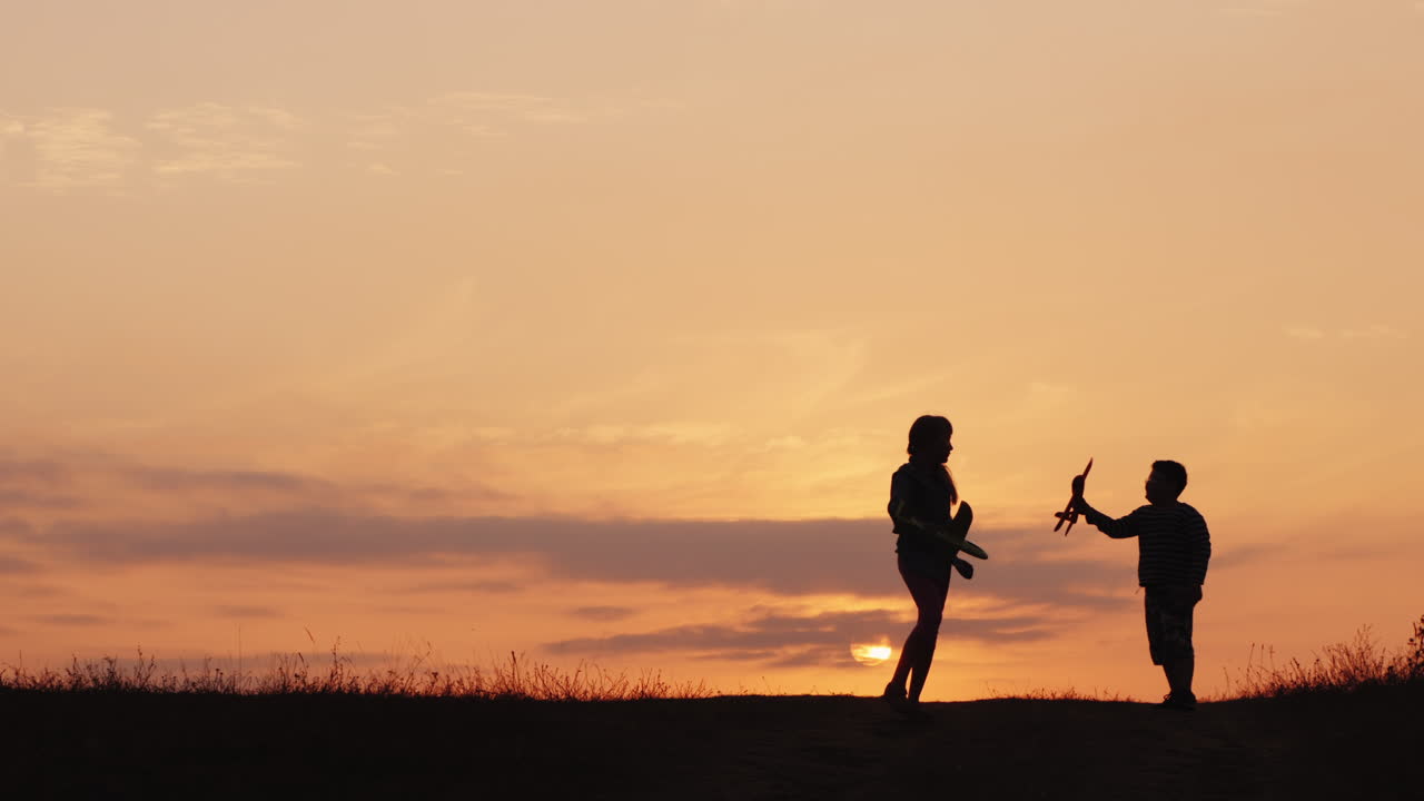 Sagome di una bambina e un bambino che giocano con gli aeroplani al tramonto. Bambini felici e spensierati.