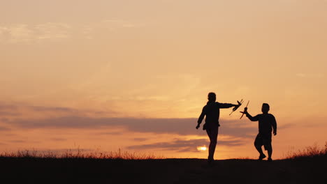 Silhouettes-Of-A-Girl-And-A-Boy-Playing-Together-With-Airplanes-At-Sunset-A-Happy-And-Carefree-Child
