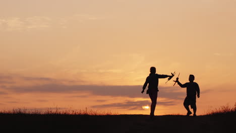 silhouettes of a girl and a boy playing together with airplanes at sunset a happy and carefree child