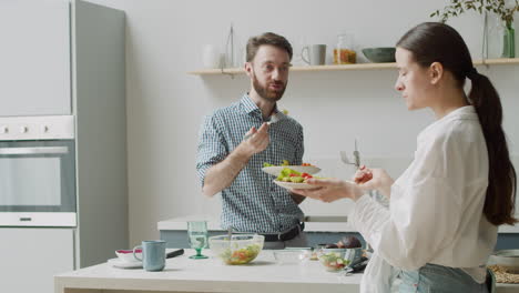 feliz pareja vegetariana comiendo una comida saludable, de pie en una cocina de estilo moderno