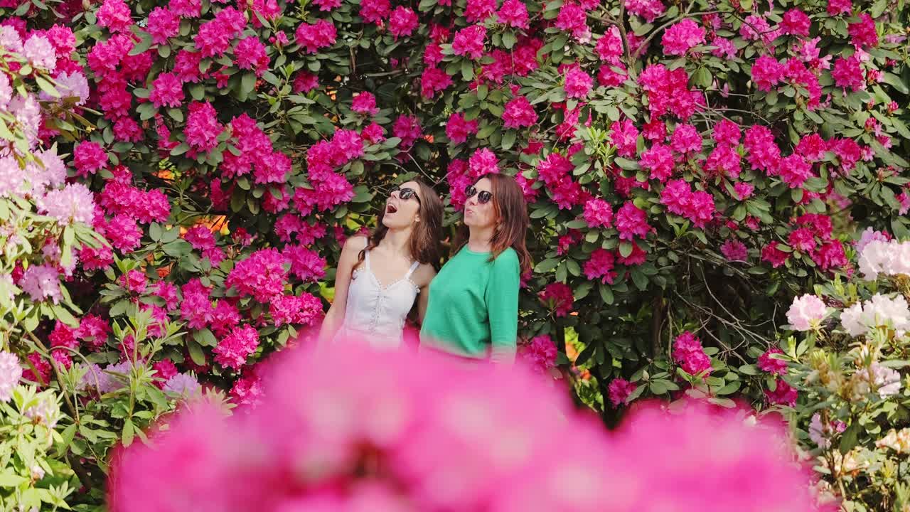 Donne con occhiali da sole che si godono un giardino fiorito sotto il sole caldo, riprese in slow motion