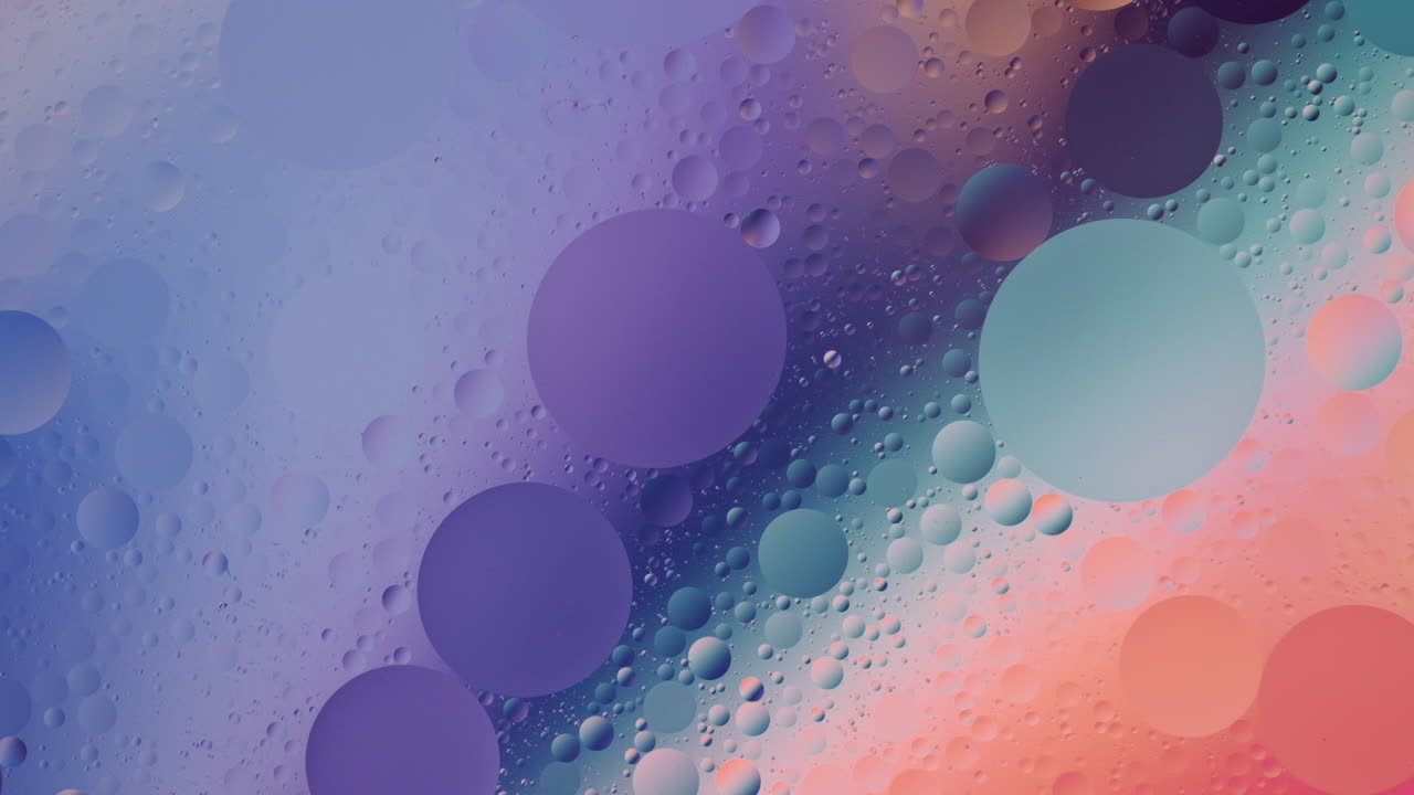 Close-up footage of oil flowing across a water surface with a colourful background