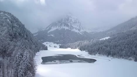 Beautiful-flight-over-a-mountain-lake-to-a-mountain-in-the-clouds-while-winter-in-Switzerland