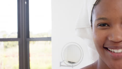 Portrait-of-happy-biracial-woman-with-towel-on-head-in-bathroom,-slow-motion