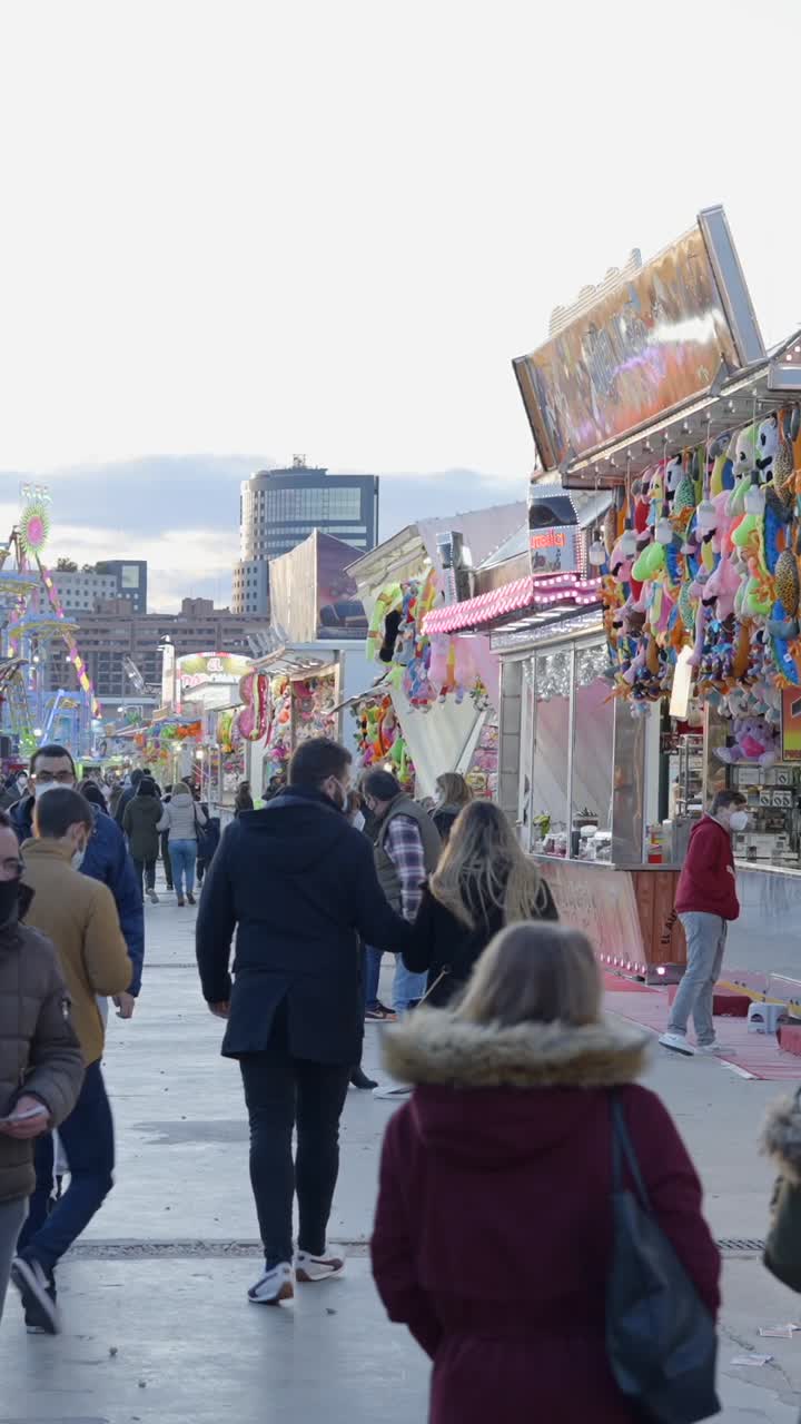 Crowd at an outdoor fair with game stalls and rides