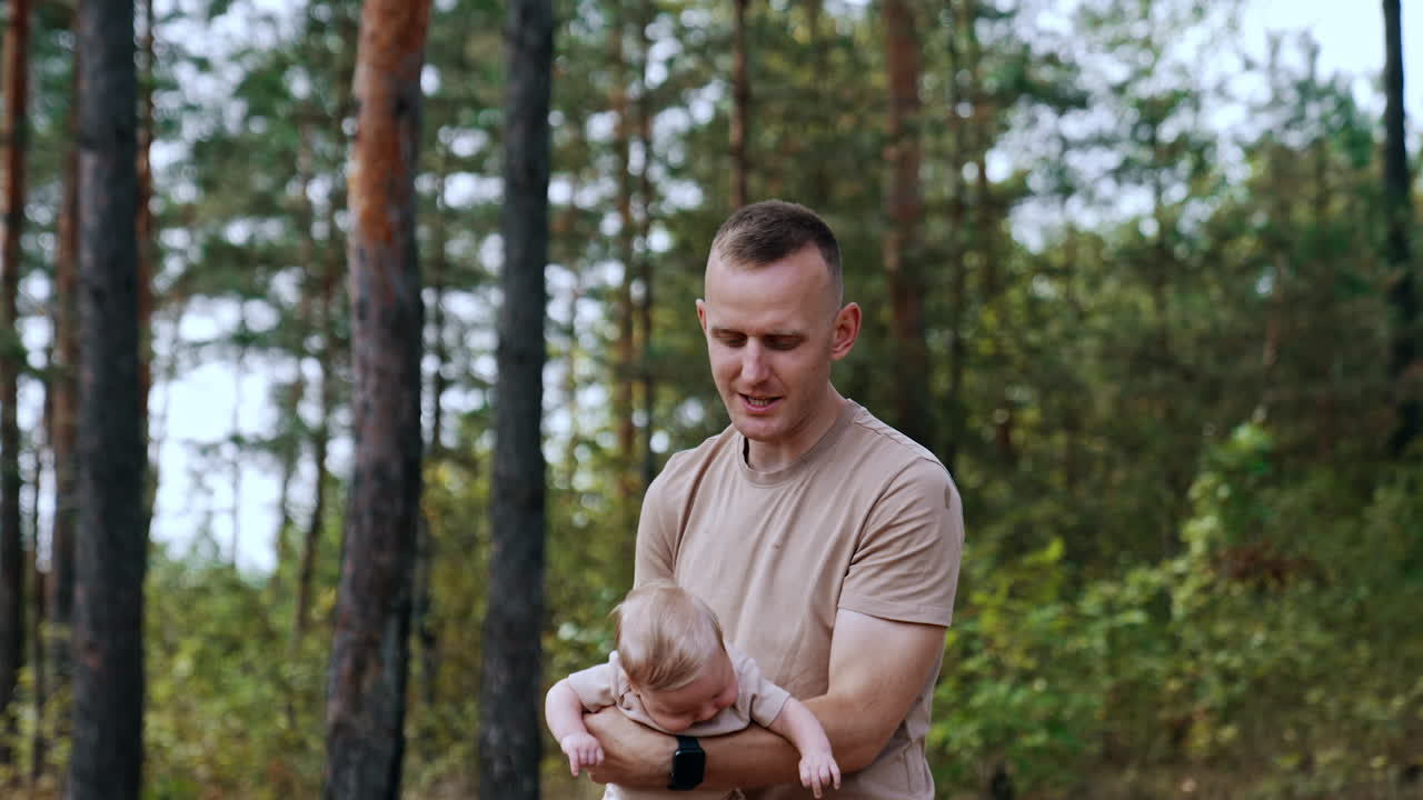 Man in beige t-shirt waves his baby boy in hands. Happy father spending time with son in nature.