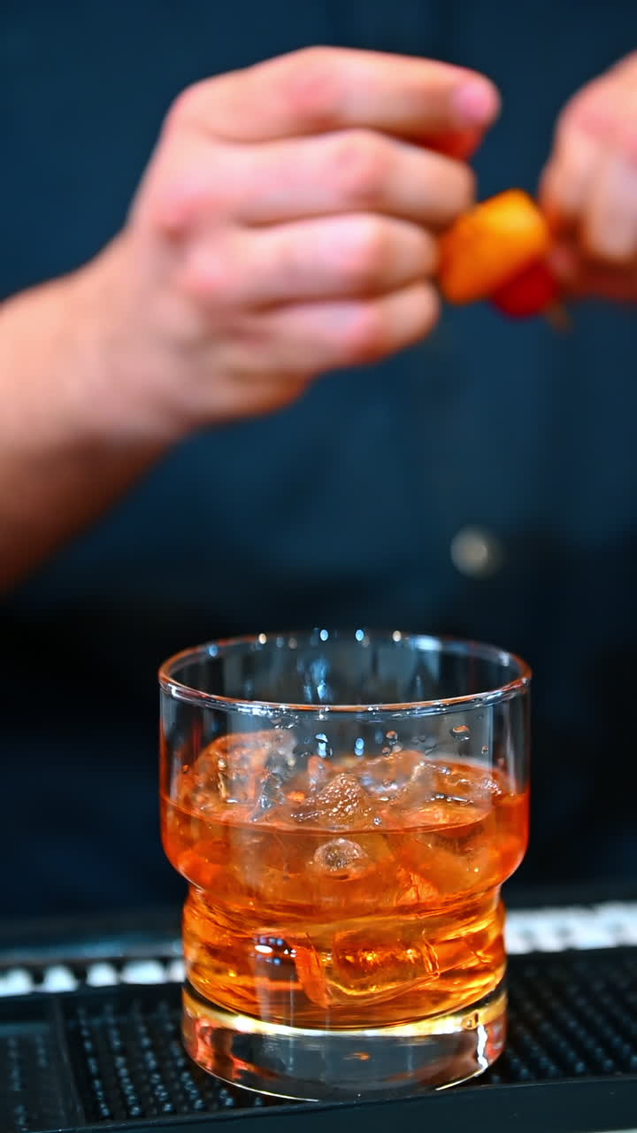 Old fashioned cocktail glass. An orange toned cocktail served over ice with a citrus garnish at the bar